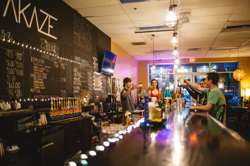 Glasses raised across the bar at night, under pendant bulbs and a string of lights along the chalkboard wall.